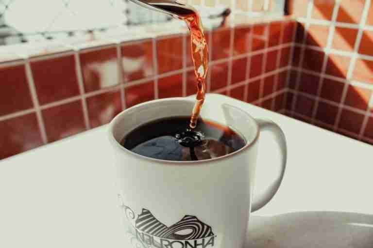 Close-up of freshly brewed coffee being poured into a stylish white mug on a tiled surface.