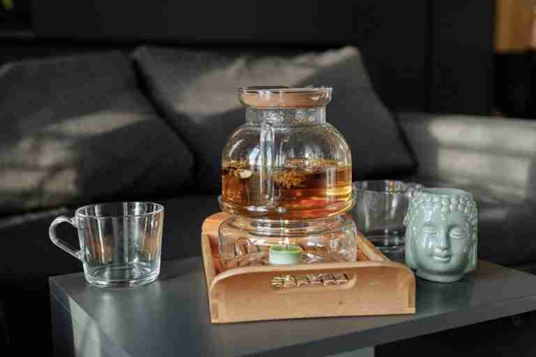 A serene still life of tea in a glass pot with a Buddha mug on a wooden tray.