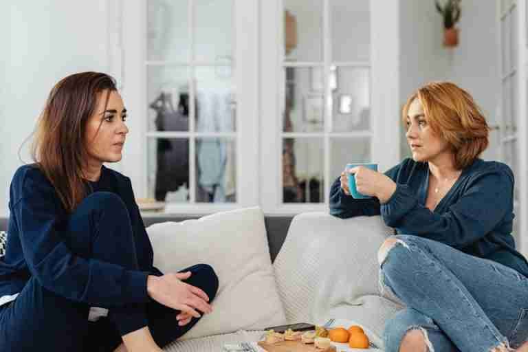 Two women enjoying a casual conversation on the couch, sipping tea and snacking indoors.