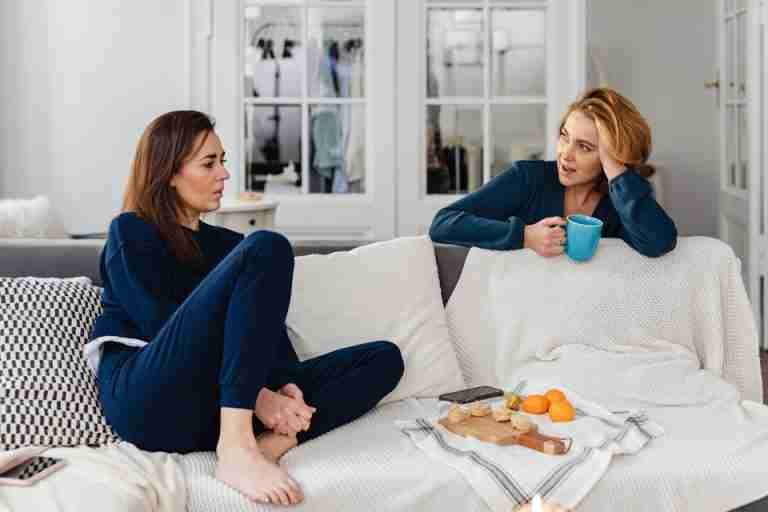 Two women having a relaxed conversation on a comfortable indoor couch.