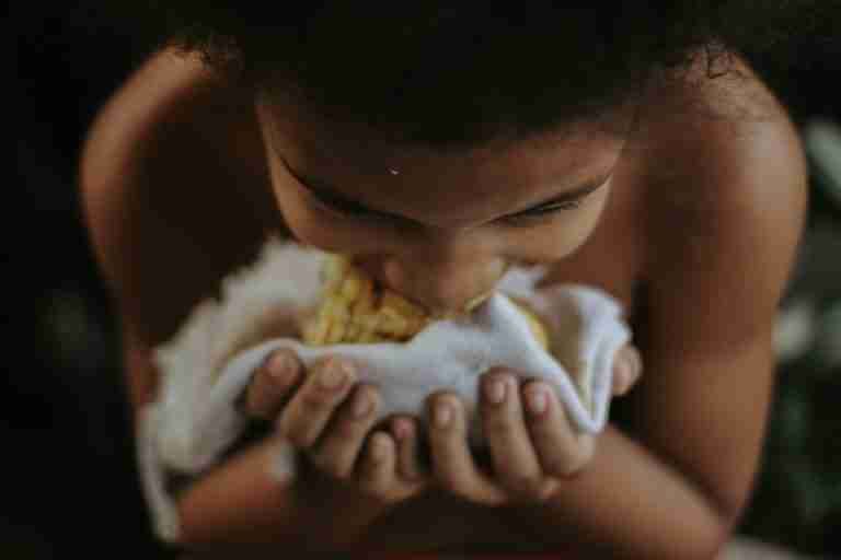 Close-up of a child eating corn, highlighting the joy of a simple meal.