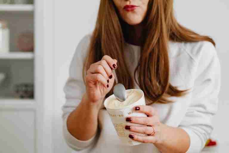 A woman with red nail polish enjoying a cup of ice cream indoors, using a spoon.
