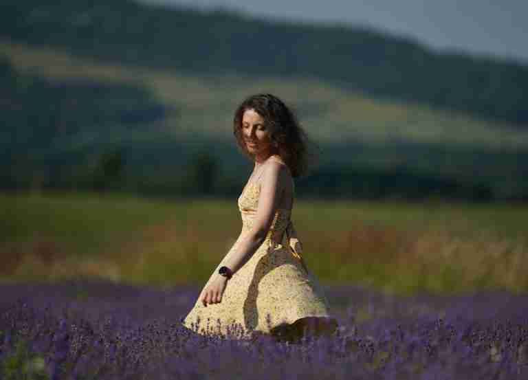 A woman in a sundress gracefully walking through a vibrant lavender field under a sunny sky.