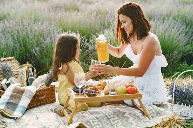 A woman pouring juice for her daughter during a picnic in a serene lavender field.