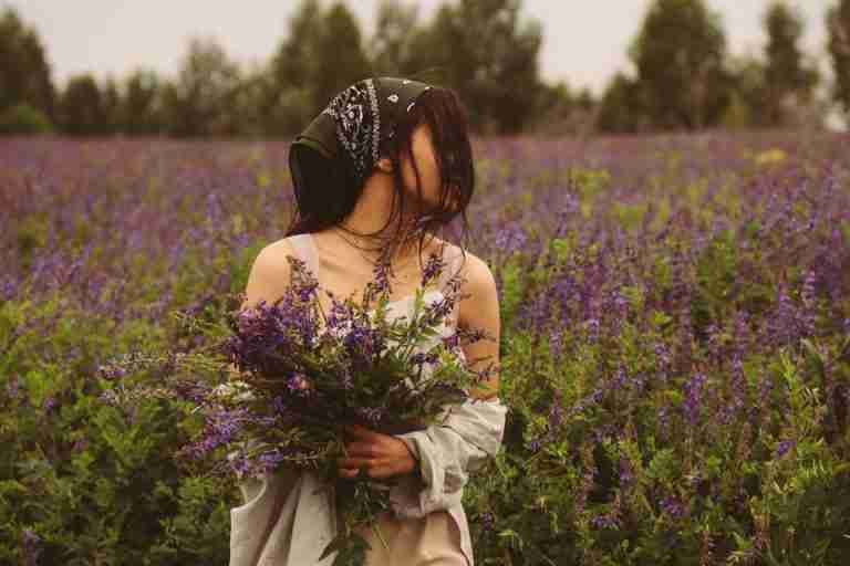 Woman with a bandana in a lavender field holding a bouquet of purple flowers.
