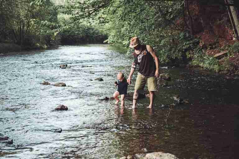 A warm moment of a father and child walking in a tranquil river surrounded by nature.