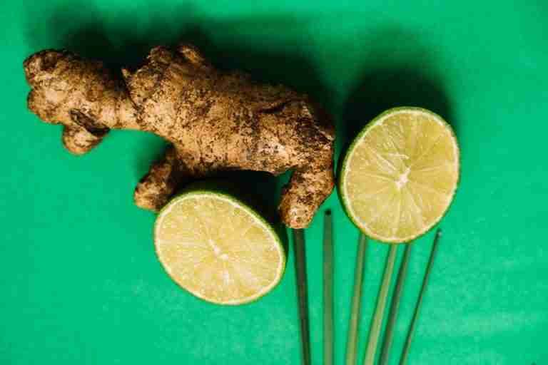Top view of fresh ginger root and lime slices on a vibrant green surface.