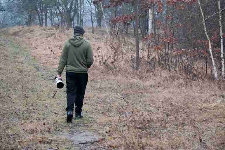 Photographer walking through a forest with camera in hand during autumn.