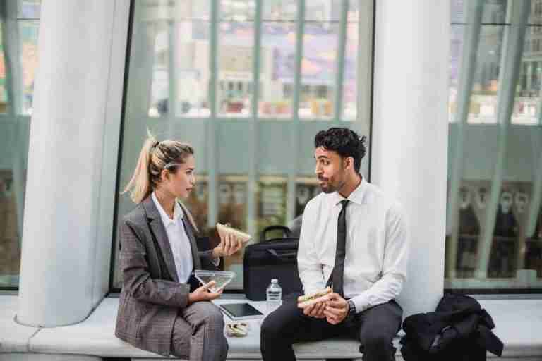 Two professionals in a modern office enjoying a lunch break and engaging in conversation.