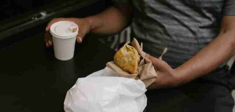 Man enjoying a casual coffee break with a hot drink and fried pastry.