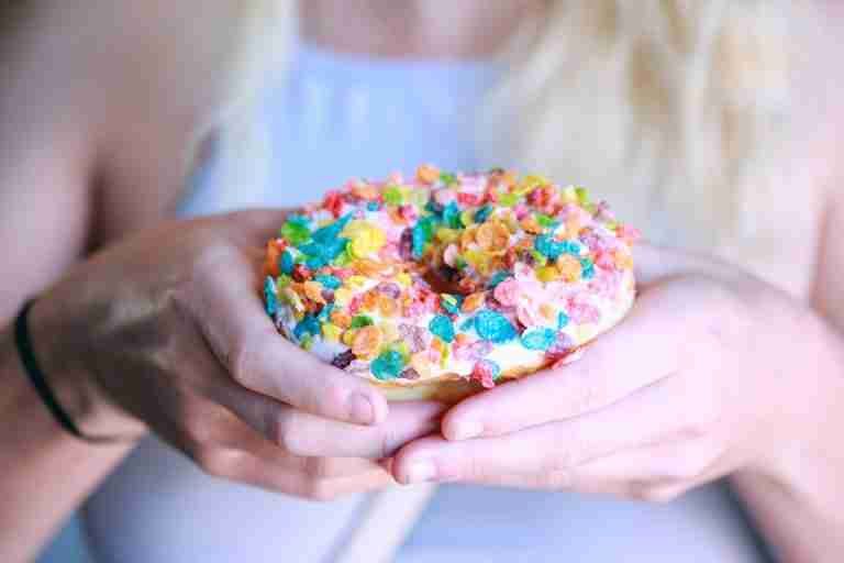 Delicious donut with colorful cereal topping being held by a person, showcasing a fun and vibrant treat.