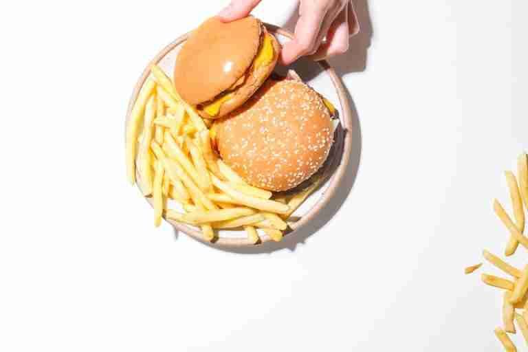 A top view of two cheeseburgers and fries on a plate, set against a white backdrop.
