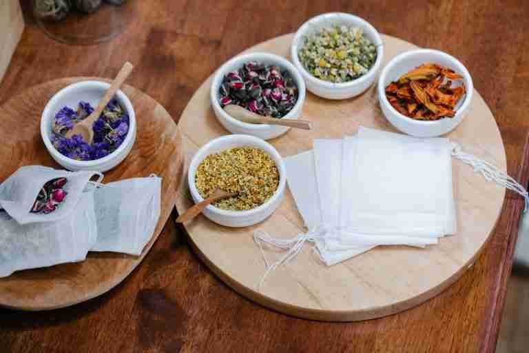 A selection of loose dried herbs and empty tea bags beautifully arranged on a wooden tray, perfect for herbal tea making.