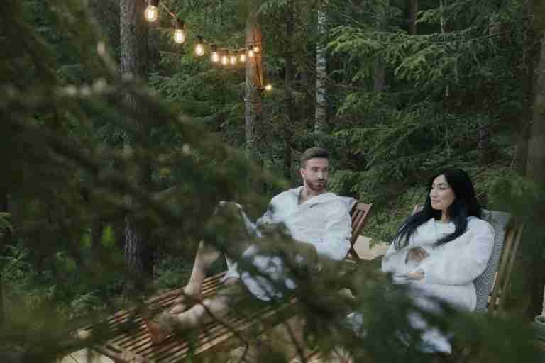 Pair relaxing in robes on wooden chairs amidst a tranquil forest setting.