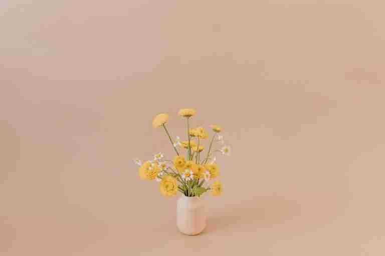 Aesthetic arrangement of yellow chamomile flowers in a vase on a beige background.
