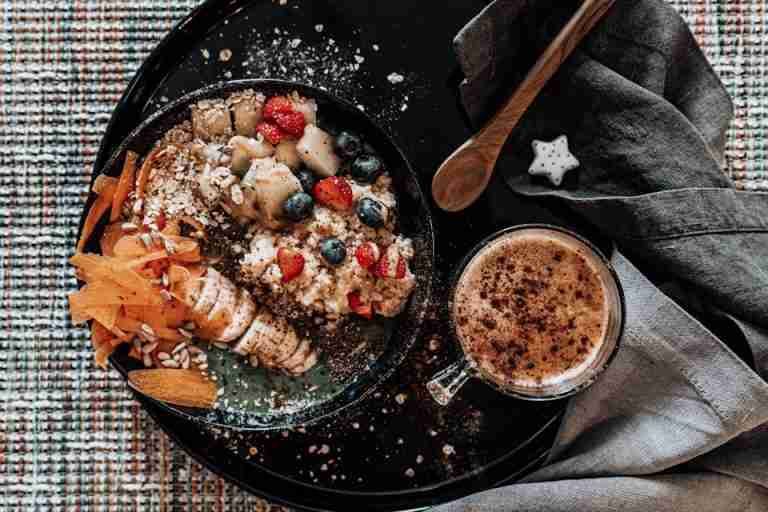 A delicious top view of a fruit and nut breakfast bowl with a fresh cup of coffee on a stylish table setting.
