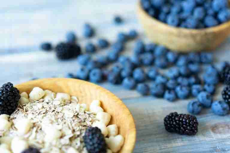 A vibrant close-up of fresh blackberries, blueberries, and oats in wooden bowls, symbolizing healthy eating.
