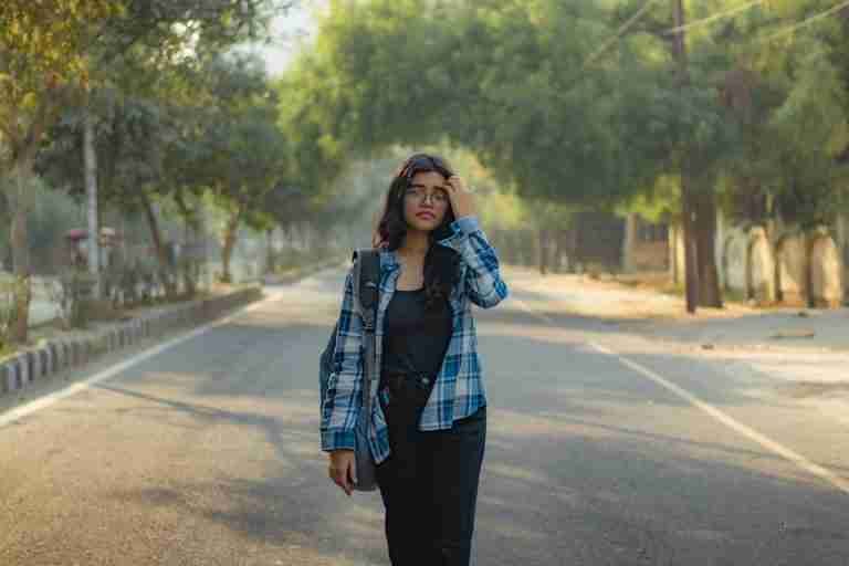 Young woman in casual attire walking down a tree-lined street, showcasing urban lifestyle and fashion.