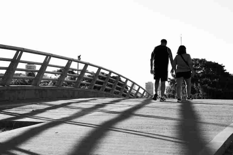 A couple walking hand in hand on a bridge, captured in a high-contrast black and white photo.