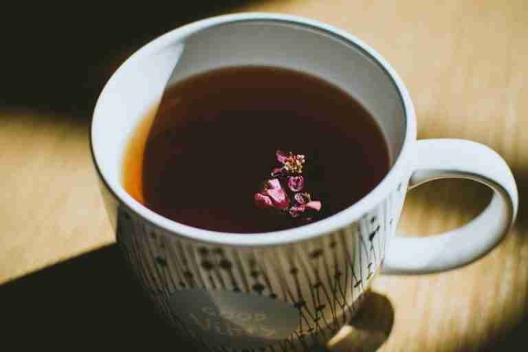 A steaming mug of herbal tea with a vibrant flower, reflecting warm light.