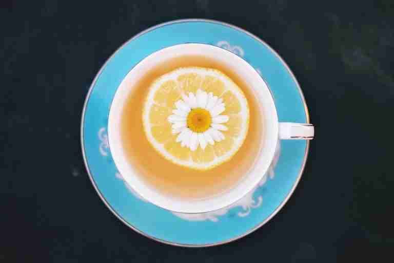 Top view of a cup of lemon tea garnished with a chamomile flower on a blue saucer.