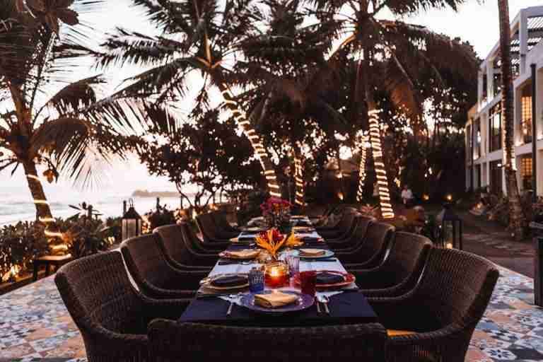 A stylish evening dining setup under illuminated palm trees at a coastal resort.