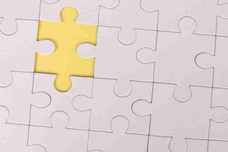 Close-up of a white jigsaw puzzle with a single yellow piece missing, symbolizing incompleteness.