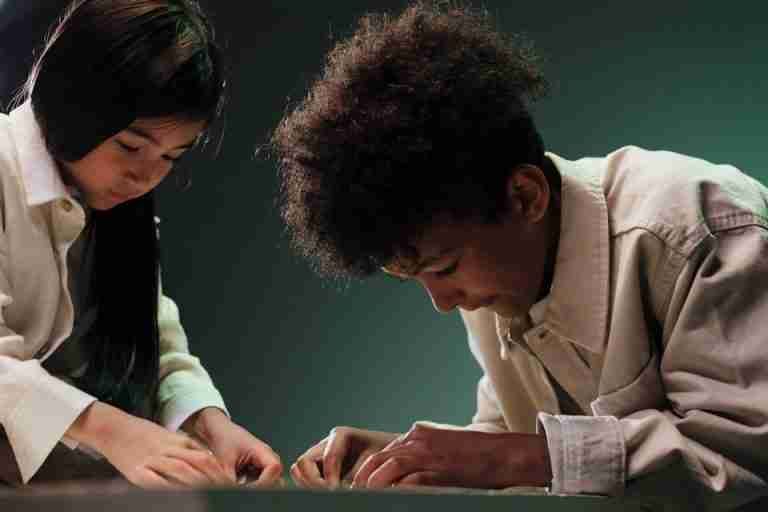 Two diverse teenagers focused on solving a puzzle together indoors.