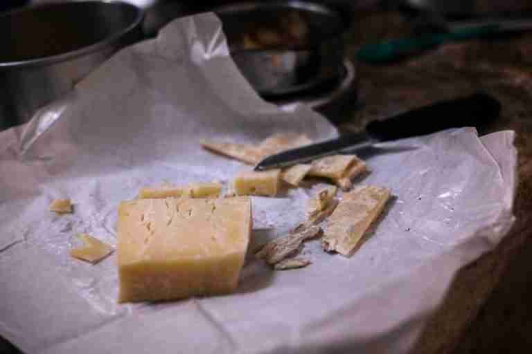 A block of cheese with slices and a knife on rustic paper, showcasing a natural and artisanal feel.