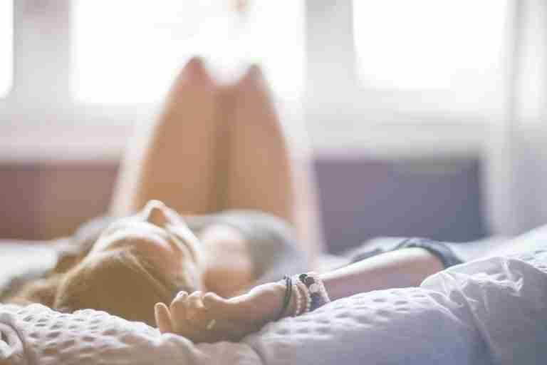 A woman lying on a bed in a peaceful, sunlit room, conveying relaxation.