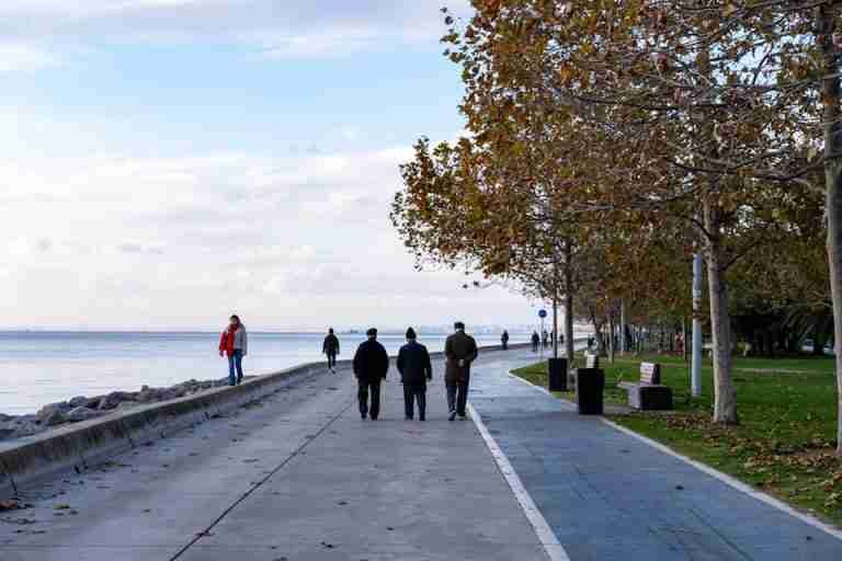 An autumn scene with people walking along the waterfront path, surrounded by trees.