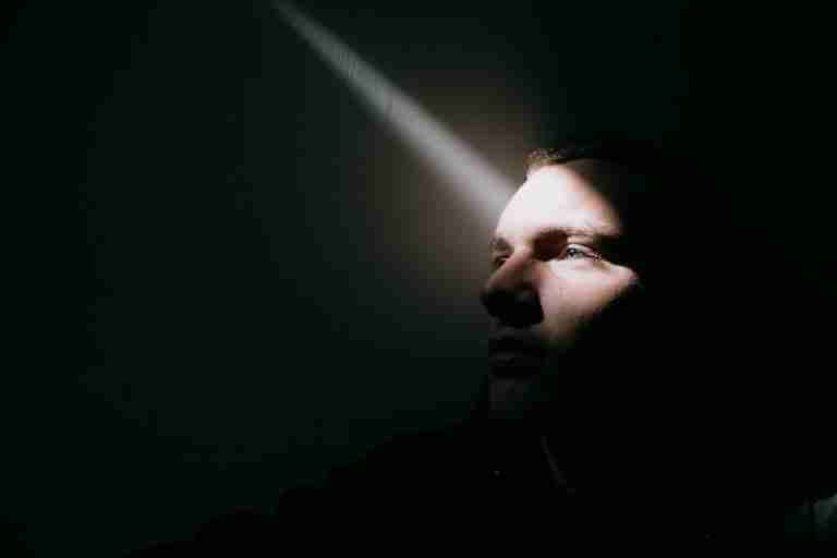 A man's face partially lit by a beam of light, evoking contemplation and mystery.