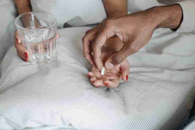 Close-up of hands offering a pill with a glass of water, symbolizing care and medication.
