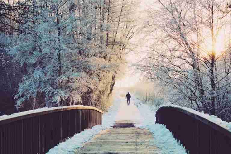 A solitary walk on a frosty bridge surrounded by snow-covered trees during sunrise.
