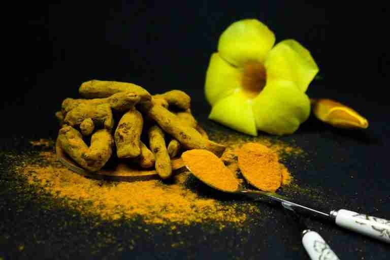 Vivid close-up of turmeric roots and powder with decorative flower on black backdrop, highlighting spice details.