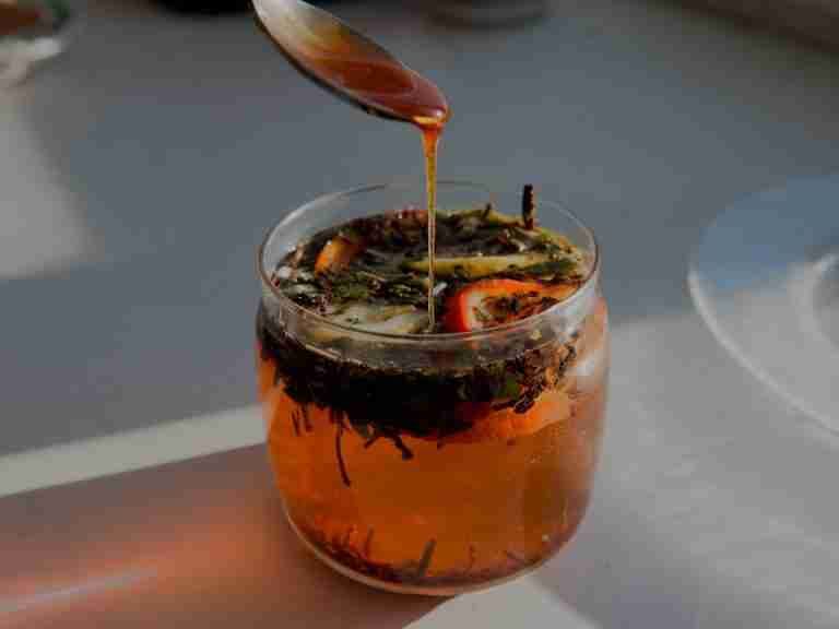 Close-up of a citrus herbal tea with honey being drizzled from a spoon, capturing warm sunlight.