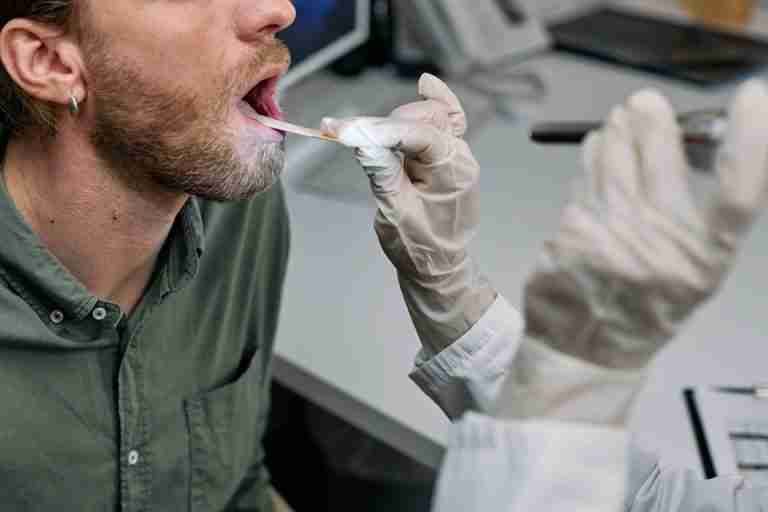 Close-up of a doctor examining a patient's throat with a tongue depressor in a clinical setting.