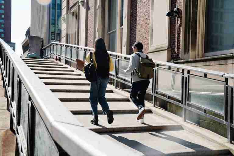 Two students walk up an outdoor staircase toward a university building.