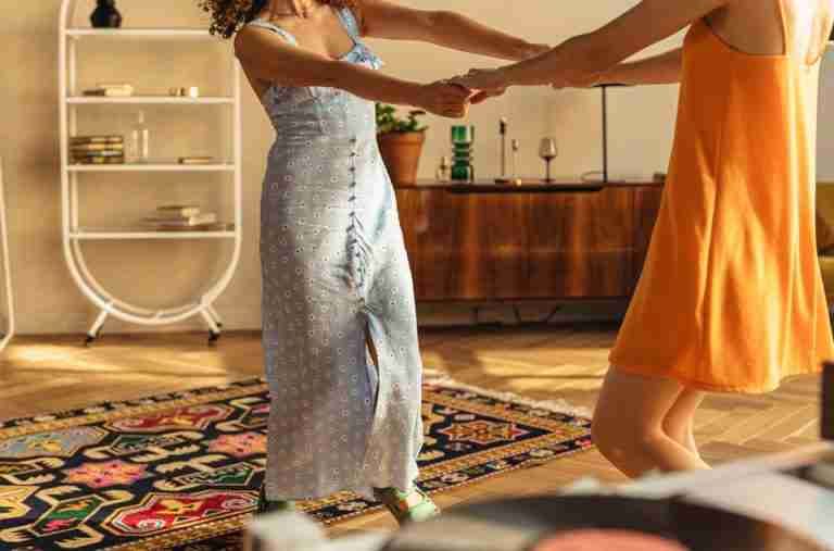 Two women gracefully dance together indoors, wearing vibrant dresses.