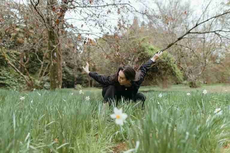 A woman performing contemporary dance in a lush spring meadow with blooming flowers.