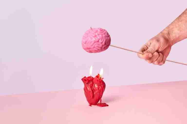 Artistic photo of a hand holding a brain-shaped candle while a heart candle burns below, symbolizing intellect vs emotion.