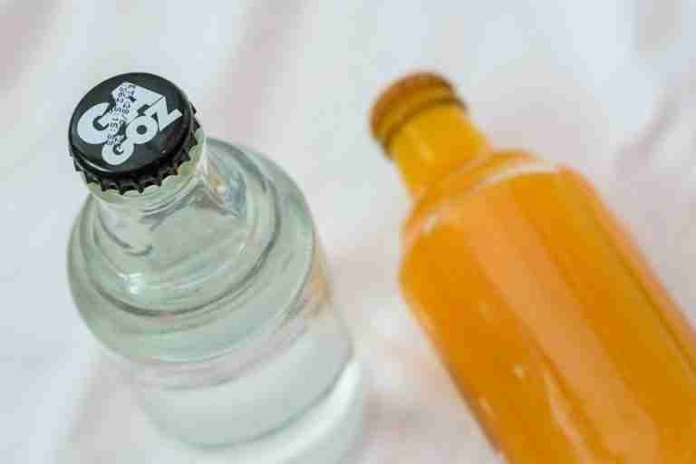 Two glass bottles with beverages, viewed from above on a white background.