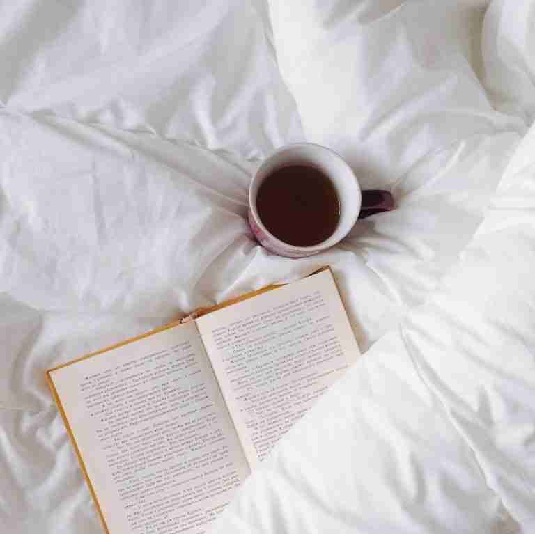 An inviting setup with a warm cup of tea and open book on white bedding, ideal for relaxation.