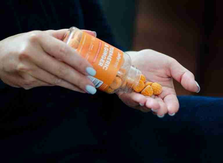 Close-up of a woman holding turmeric ginger gummies in hand, promoting a health supplement.