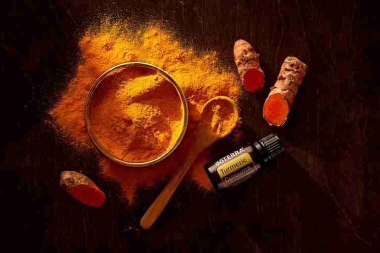 Top view of turmeric powder, curcuma roots, and essential oil on wooden surface.