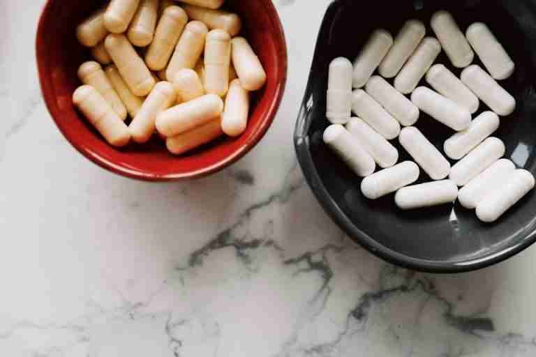 Top view of red and black ceramic bowls filled with assorted capsules on marble surface.