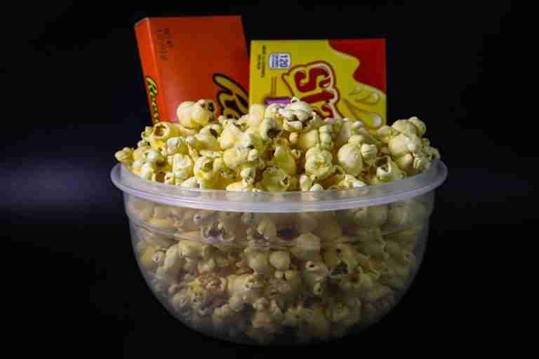 A bowl of popcorn with chocolate candy boxes, ideal for movie night themes and snack adverts.