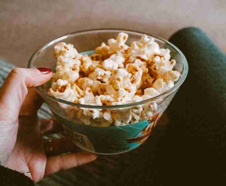 Close-up of a hand holding a glass bowl filled with delicious popcorn. Perfect snack time capture.