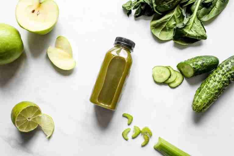 Discover fresh green juice surrounded by spinach, cucumber, apple, and lime.