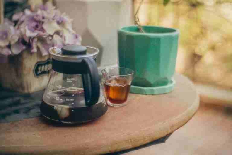 Cozy outdoor scene featuring a V60 coffee setup with iced coffee, a green planter, and flowers.